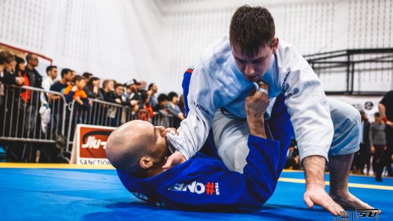Adult Brazilian Jiu-Jitsu students practicing guard control in a Gi during live training at a BJJ class.